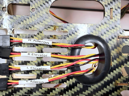 Close-up of a model airplane control surface setup with wiring and labels on a carbon fiber frame.