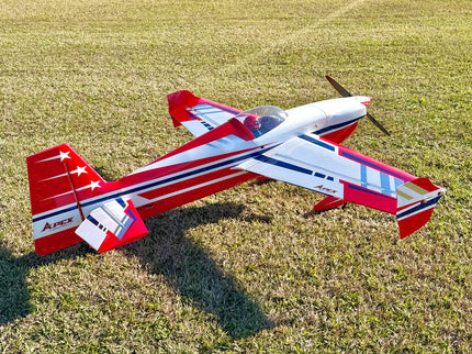 A red, white, and blue remote control airplane with a three-blade propeller, resting on a grassy field.