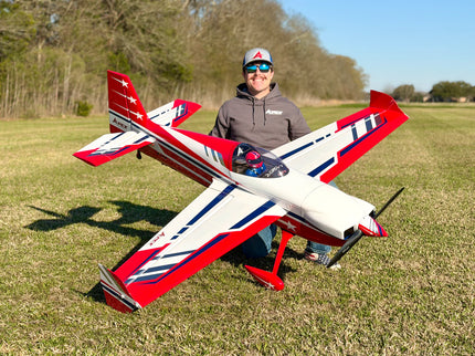 Person holding a red, white, and blue model airplane in an open field.