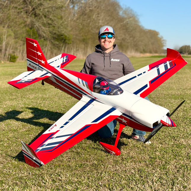 Person holding a red, white, and blue model airplane in an open field.