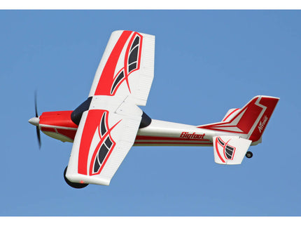 Red and white model airplane with black accents flying against a clear blue sky.