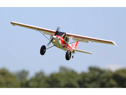 Small airplane flying against a clear blue sky with trees below.