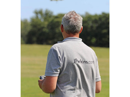 Man in a gray shirt with 'JPerkins.com' logo watching a small airplane fly by.