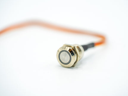 Close-up of a gold-colored sensor with a black cable on a white background