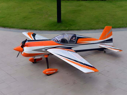Orange and white model airplane on a paved surface with grass in the background