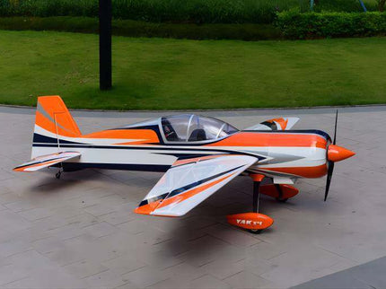 Orange and white model airplane on a paved surface with grass in the background