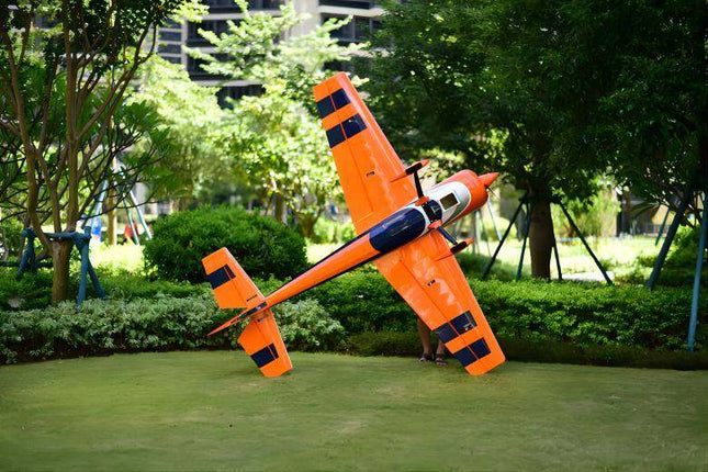Orange toy airplane on a grassy area with trees in the background