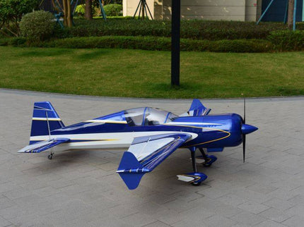 Blue and white model airplane on a paved surface with grass and trees in the background