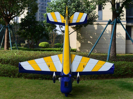 Model airplane with yellow and blue design on a grassy area with trees and buildings in the background