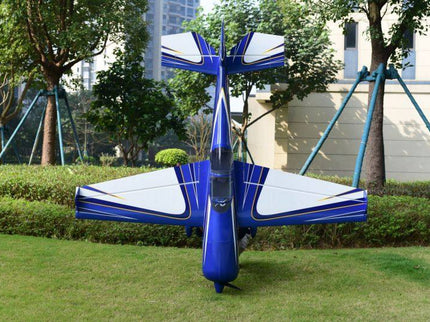 Blue and white model airplane on grass with trees and buildings in the background