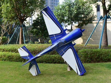 Blue and white model airplane on grass with trees and buildings in the background