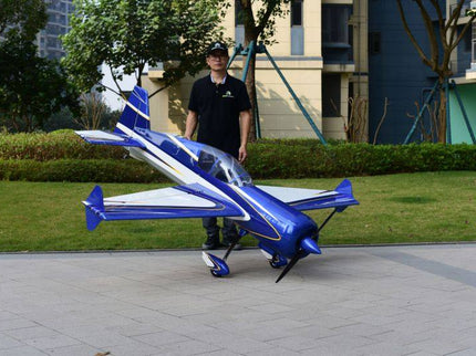 Man standing next to a blue and white model airplane on a paved area with greenery in the background.