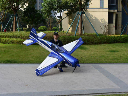 Person holding a large blue and white model airplane outdoors on a paved area with greenery.