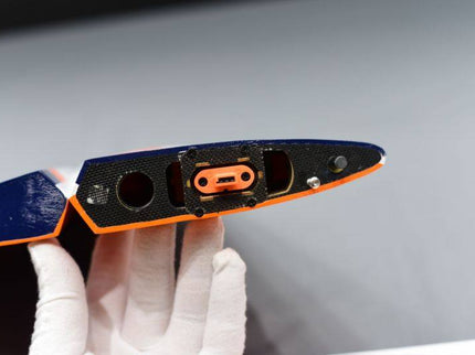 Hand holding a black and orange object with a white glove on a gray background