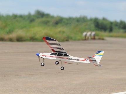 Phoenix Model Domino 62” Trainer Model airplane on a runway with trees in the background