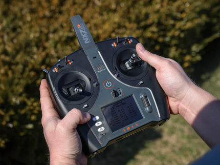 Person holding a black radio control transmitter with a blurred natural background