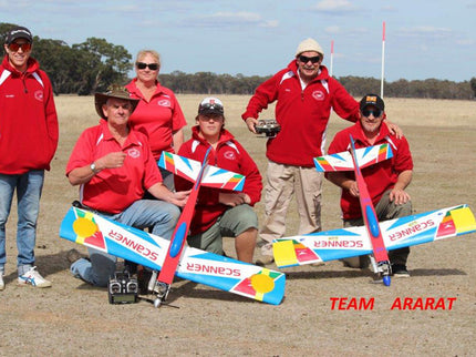 Group of people in red jackets with Phoenix Model PH006-SCANNER 57" model airplanes on a plain background