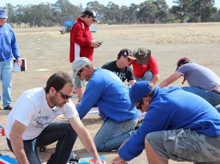 Group of people gathered around a Phoenix Model PH006-SCANNER 57" airplane on a grassy field