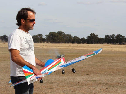 Man holding a colorful Phoenix Model PH006-SCANNER 57" model airplane in an open field