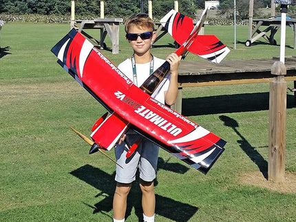 Boy holding a large red and black model airplane in an outdoor setting