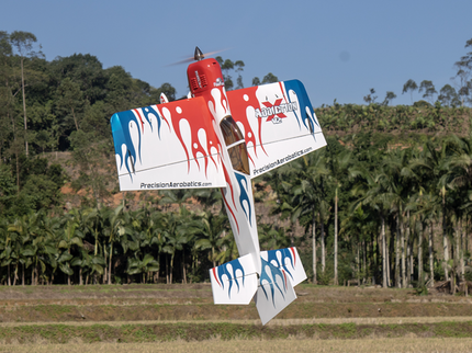 Red, white, and blue airplane with branding flying over a forested area.