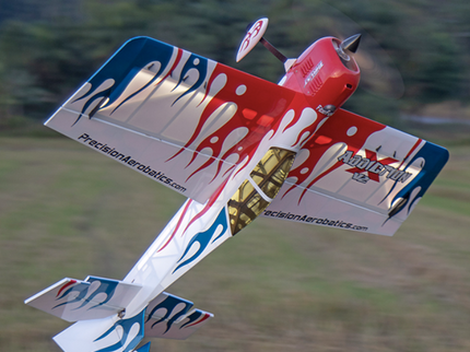 Colorful model airplane with branding flying over a grassy field