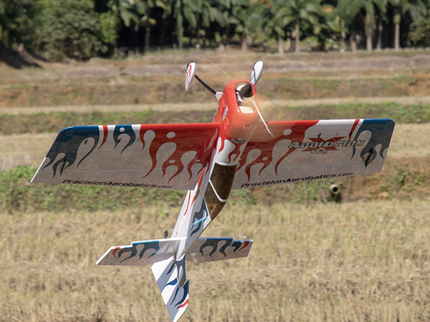 Model airplane flying over a grassy field with trees in the background