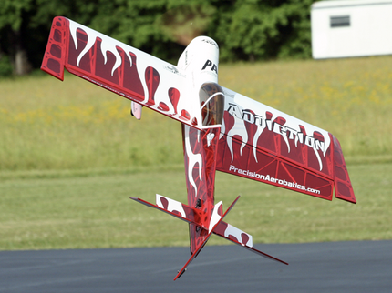 Red and white model airplane with 'Precision Aerobatics' branding on a grassy field.