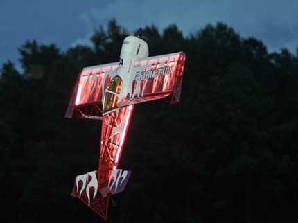 Neon sign of a stylized airplane with flames against a dark background