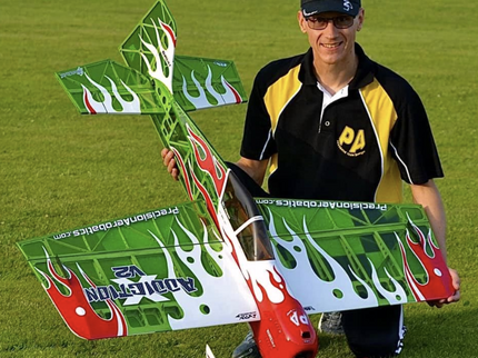 Man holding a green and red model airplane on grass