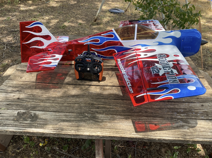 Red and blue RC airplane with flame design on a wooden table outdoors.