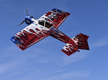 Red and white airplane with blue accents flying against a clear blue sky.