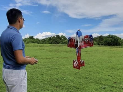 Man flying a red and white kite in an open field with a blue sky and clouds.