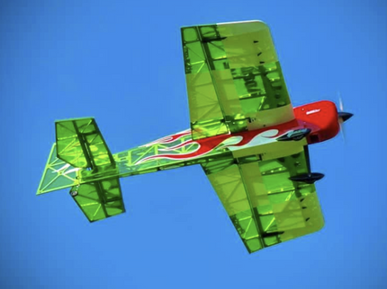 Green and red model airplane flying against a clear blue sky