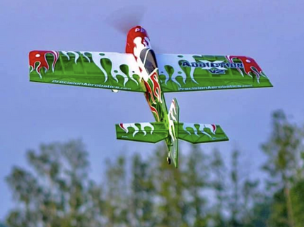 Colorful model airplane flying against a clear sky with trees below.