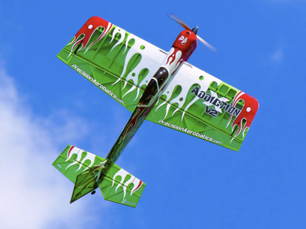 Green and red model airplane flying against a blue sky