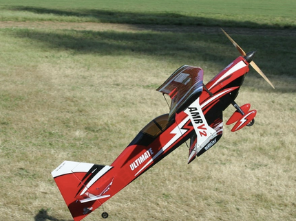 Red and black model airplane flying over a grassy field