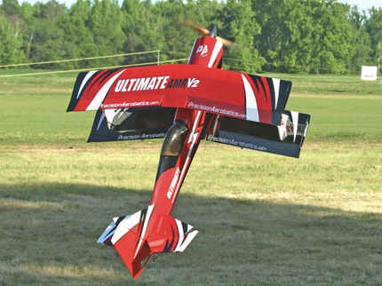 Red and black model airplane with 'Ultimate' branding in a grassy field.