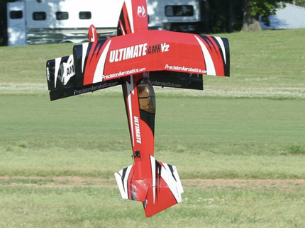 Red and black model airplane on a grassy field with trees in the background