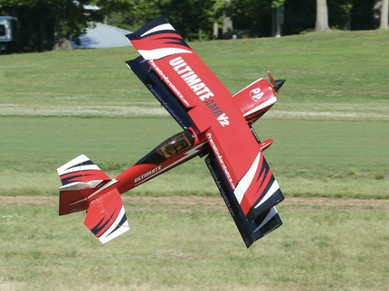 Red and black model airplane flying over a grassy field