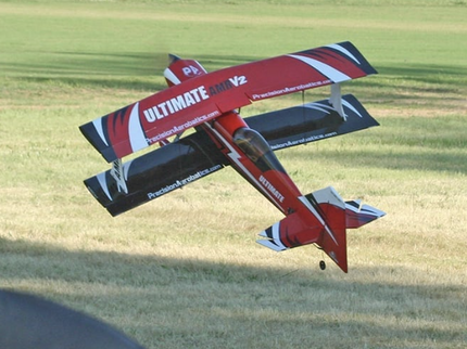 Red and black model airplane flying over a grassy field