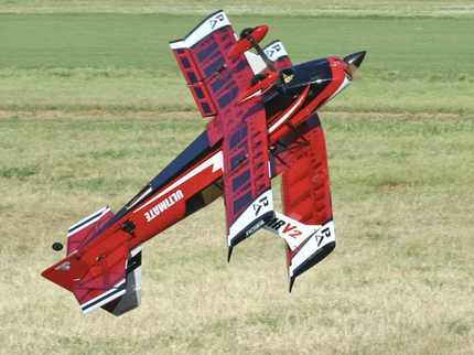 Red and black model airplane on a grassy field