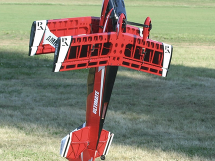Red and white model airplane on a grassy field