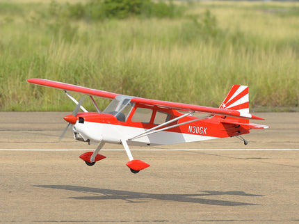 Red and white Phoenix Model DECATHLON model airplane on a runway with grass in the background
