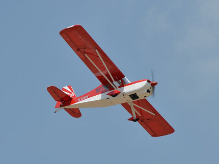 Red and white Phoenix Model DECATHLON airplane flying against a clear blue sky
