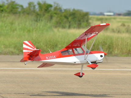 Red and white Phoenix Model DECATHLON airplane on a runway with grass and trees in the background