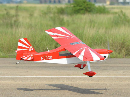 Red and white Phoenix Model DECATHLON model airplane on a runway with grass in the background