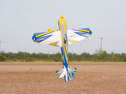 Phoenix Model EDGE 540 V3 67'' ARF V2 (20-26cc) Model airplane in flight over a field with power lines and trees in the background