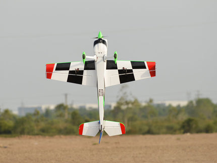 Phoenix Model SBACH 342 60'' ARF V2  Model airplane with checkered pattern flying over a field with trees in the background