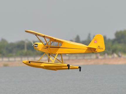 Yellow Phoenix Model PIPER J3 CUB  seaplane flying over a water runway with trees in the background
